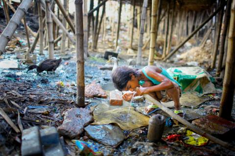 Image of child drinking water from pipe near garbage 